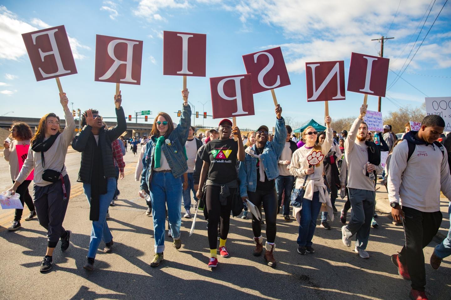 marchers hold up signs that read "INSPIRE" during the MLK March